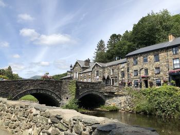 Arch bridge over river by buildings against sky