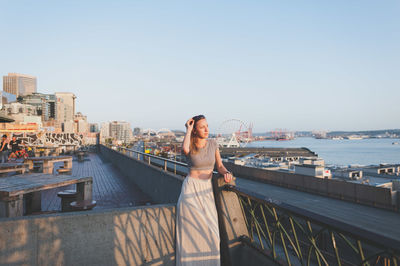 Woman standing on railing by sea against clear sky