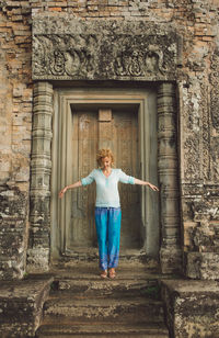 Mid adult woman with arms outstretched standing in historic building