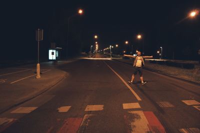 Young man with arms outstretched screaming while standing on road at night