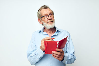 Smiling senior man holding diary looking away against white background