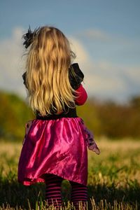 Rear view of girl standing on field against sky