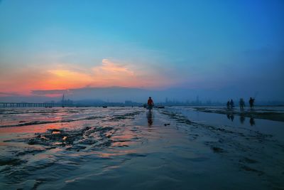 Men standing on beach against sky during sunset