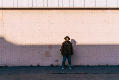 Young woman wearing hat and overcoat standing in front of brick wall