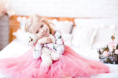 Girl embracing teddy bear sitting on bed