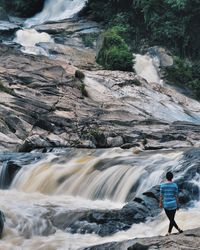 Man standing on rock against waterfall