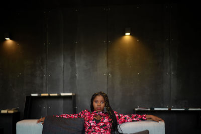 African american female in bright pink dress sitting on couch in hotel lobby and looking at camera