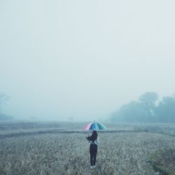 Rear view of man standing on field during rainy season