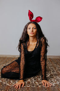 Portrait of beautiful young woman sitting against red wall