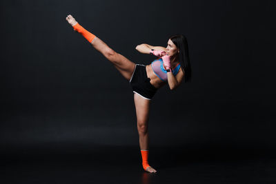 Young woman with arms raised standing against black background