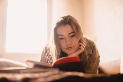 Young woman reading book while lying on bed at home