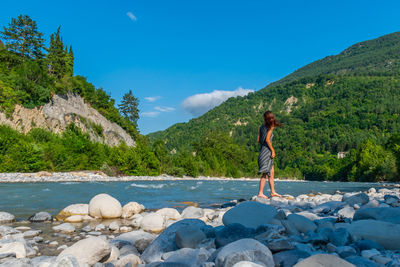 Woman standing on rock by mountain against sky