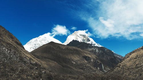 Low angle view of snowcapped mountains against blue sky