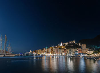 Illuminated buildings by sea against sky at night