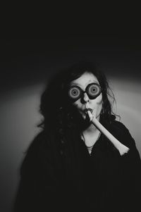 Woman wearing novelty glasses blowing party horn while standing against wall