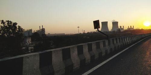 Road by buildings against sky during sunset