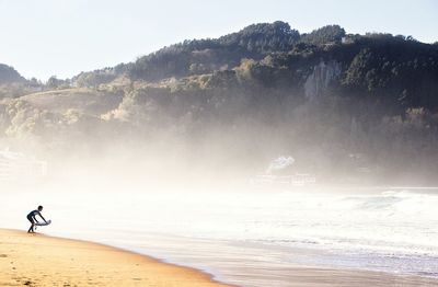 Man with surfboard at beach by mountain