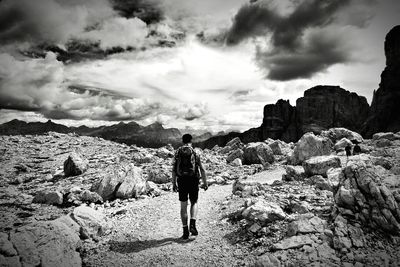 Man standing on rock formation against cloudy sky