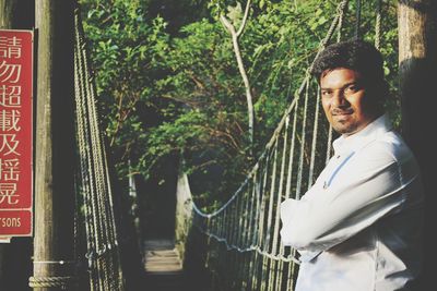 Portrait of man standing by suspension footbridge