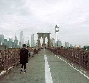 Rear view of man standing on bridge against buildings in city