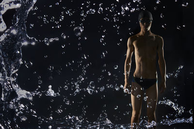 Water splashing against shirtless swimmer against black background