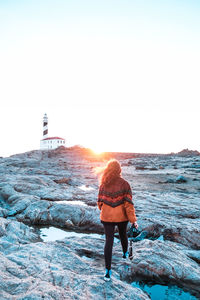 Rear view of man standing on rock in sea against sky