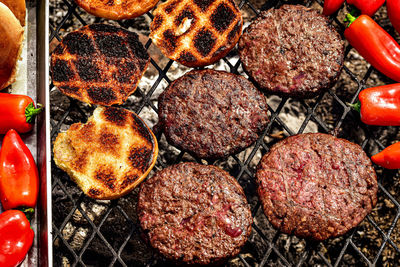 Grilling hamburger patties, bread buns, red chili peppers on outdoor grill 