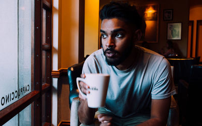 Thoughtful man holding coffee cup and looking through window in cafe