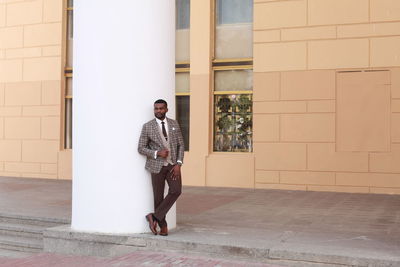 Full length portrait of young man standing against building