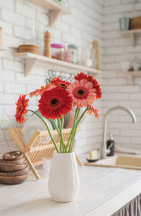 Rustic kitchen interior with white brick wall and white wooden shelves. fresh gerbera flowers