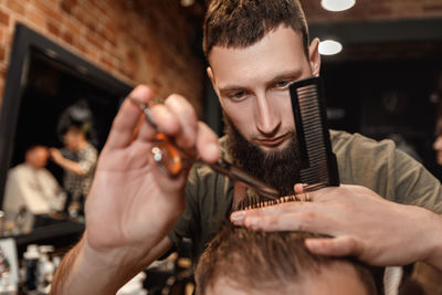 Male barber cutting hair of customer in salon