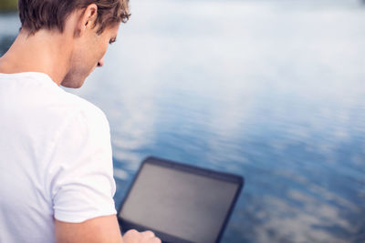 Rear view of mature man using laptop by lake