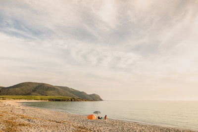 People sitting at beach against cloudy sky during sunset