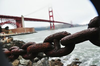 Close-up of rusty chain against golden gate bridge on san francisco bay