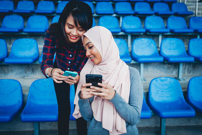 Full length of young woman using phone while sitting outdoors