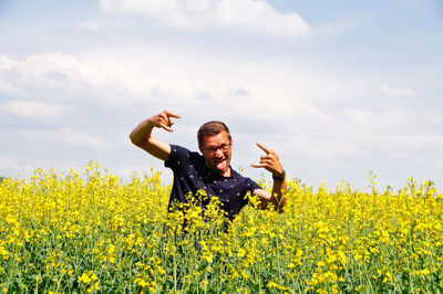 Portrait of happy mid adult man gesturing on oilseed rape field against cloudy sky