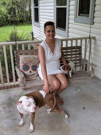 Portrait of young woman stroking dogs while sitting on swing at porch