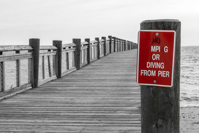 Information sign on wooden post by sea against clear sky