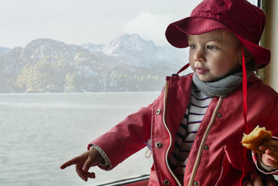 Toddler dressed in coat and hat optioning and looking away. lake and mountain scenic background. 