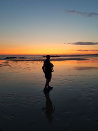 Silhouette man standing on beach against sky during sunset