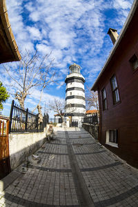 Narrow pathway leading towards tower against blue sky