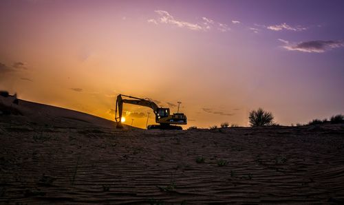 Excavator on sandy field against sky during sunset