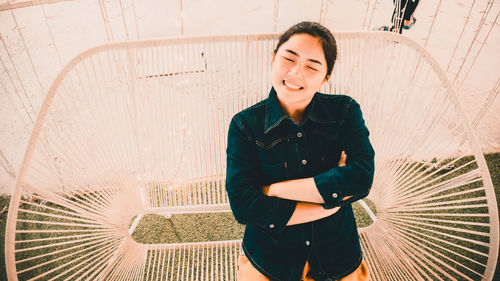 High angle view of smiling young woman with arms crossed sitting on swing