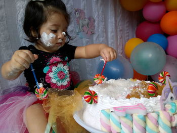 Close-up of messy baby girl eating cake at home during birthday