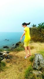 Full length of young woman standing in sea against clear sky