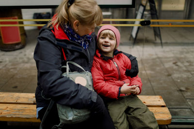 Grandmother with smiling grandson sitting on bench in city