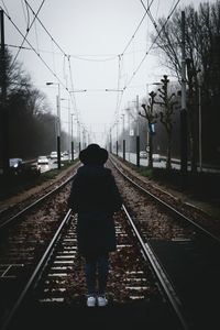 Rear view of man on railway tracks against clear sky