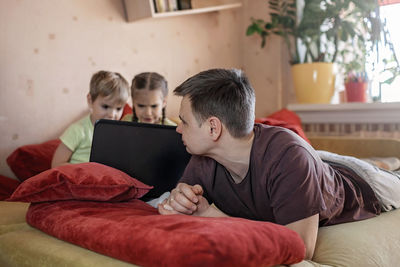 Rear view of friends sitting on laptop at home