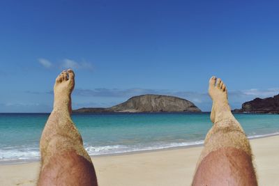 Midsection of man on beach against blue sky