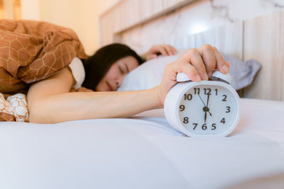 Close-up of woman holding alarm clock while lying on bed at home